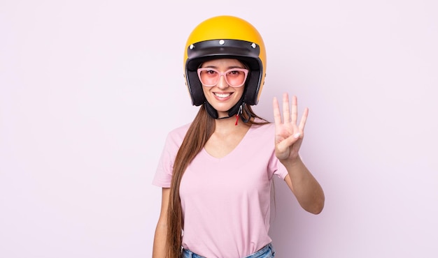 Mulher jovem e bonita sorrindo e parecendo amigável, mostrando o número quatro. piloto de moto e capacete