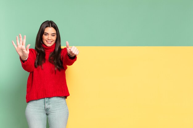 Mulher jovem e bonita sorrindo e parecendo amigável, mostrando o número seis ou sexto com a mão para a frente, em contagem regressiva