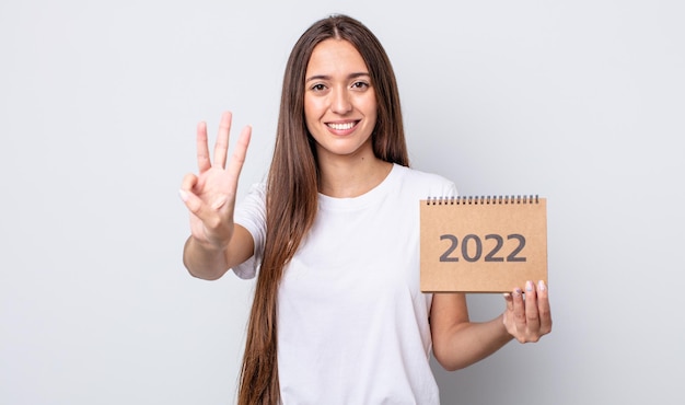 Mulher jovem e bonita sorrindo e parecendo amigável, mostrando o número três. Conceito de planejador 2022