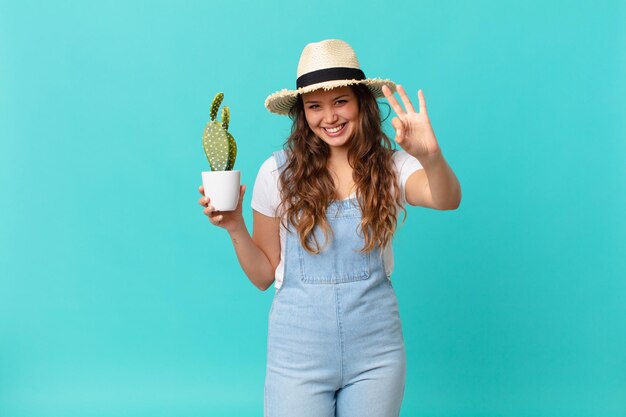 Mulher jovem e bonita sorrindo e parecendo amigável, mostrando o número três e segurando um cacto