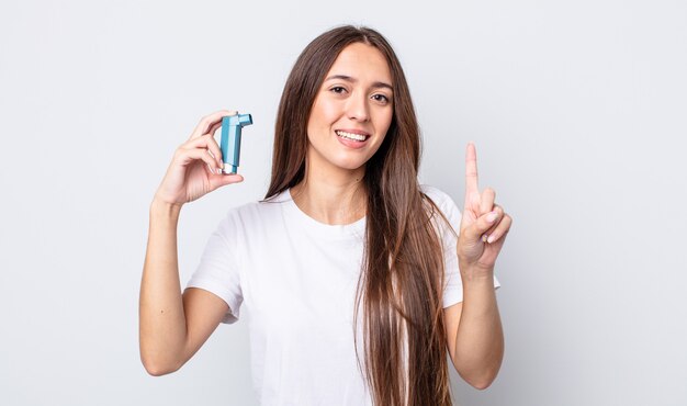 Mulher jovem e bonita sorrindo e parecendo amigável, mostrando o número um. conceito de asma