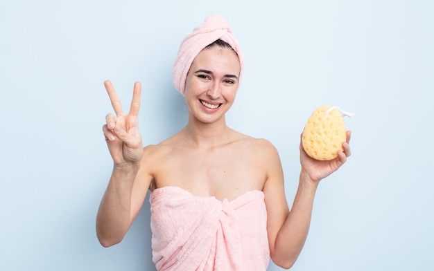 Mulher jovem e bonita sorrindo e parecendo feliz, gesticulando vitória ou paz. conceito de chuveiro e esponja