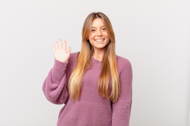 Mulher jovem e bonita sorrindo feliz, acenando com a mão, dando as boas-vindas e cumprimentando você