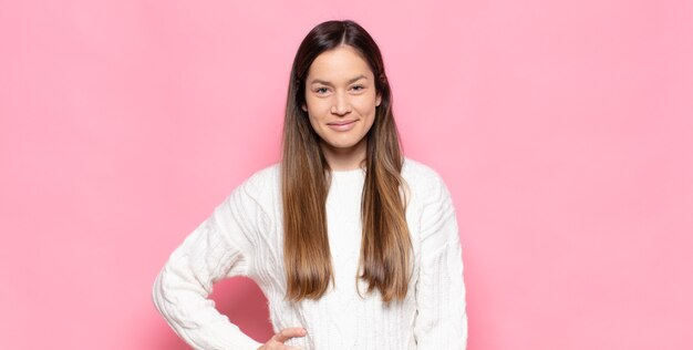 Mulher jovem e bonita sorrindo feliz com uma mão no quadril e uma atitude confiante, positiva, orgulhosa e amigável