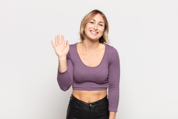 Mulher jovem e bonita sorrindo feliz e alegre, acenando com a mão, dando as boas-vindas e cumprimentando você ou dizendo adeus