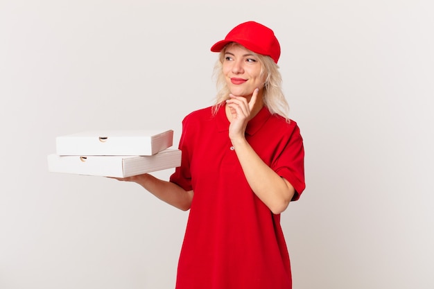 Mulher jovem e bonita sorrindo feliz e sonhando acordada ou duvidando. conceito de entrega de pizza