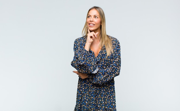 Mulher jovem e bonita sorrindo feliz e sonhando acordada ou duvidando, olhando para o lado