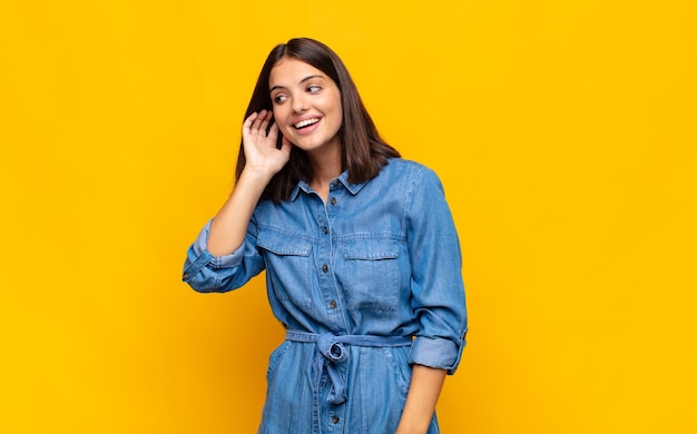 Mulher jovem e bonita sorrindo, olhando curiosamente para o lado isolado