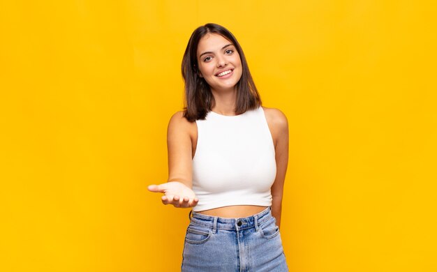 Mulher jovem e bonita sorrindo, parecendo feliz, confiante e amigável, oferecendo um aperto de mão para fechar um negócio, cooperando