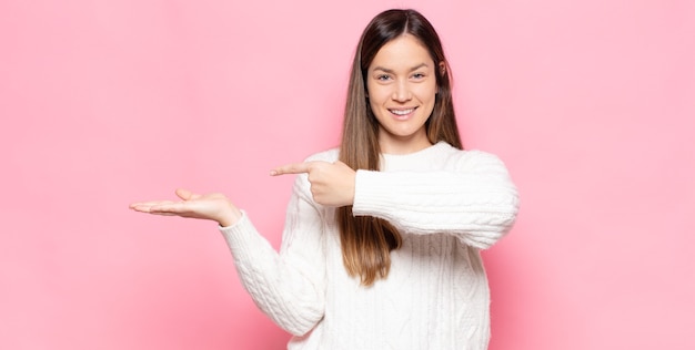 Mulher jovem e bonita sorrindo, sentindo-se feliz, despreocupada e satisfeita, apontando para um conceito ou ideia no espaço da cópia ao lado