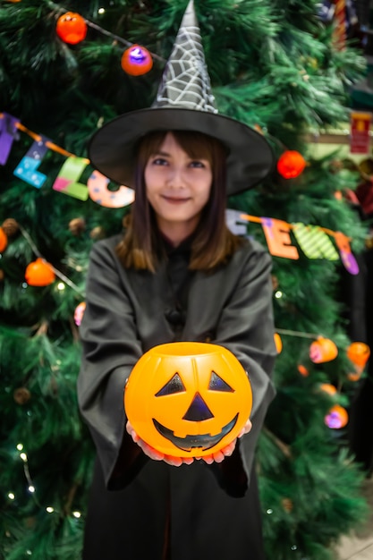 Mulher jovem e bonita surpresa ou estilo escuro de bruxa de Halloween com segurando uma abóbora no Halloween comemorar festa à noite.