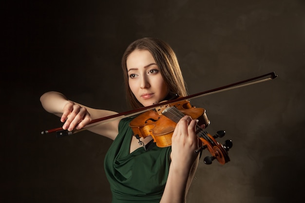 Mulher jovem e bonita tocando violino sobre fundo preto