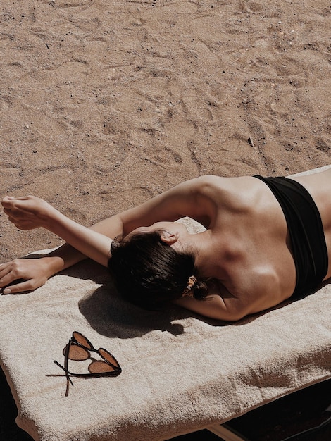 Foto mulher jovem e bonita toma sol na praia óculos de sol femininos na toalha bege estilo de vida estético mínimo revista de blog de moda mídia social tome banho de sol relaxe relaxe nas férias de viagem de verão