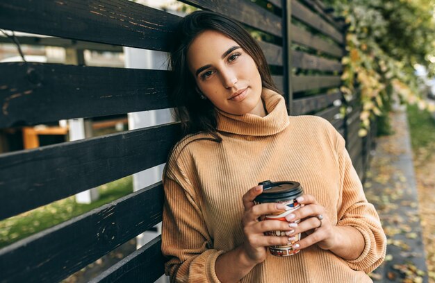 Mulher jovem e bonita tomando café em movimento na rua da cidade Linda mulher na rua da cidade bebendo cappuccino quente Menina bonita morena com uma xícara de café