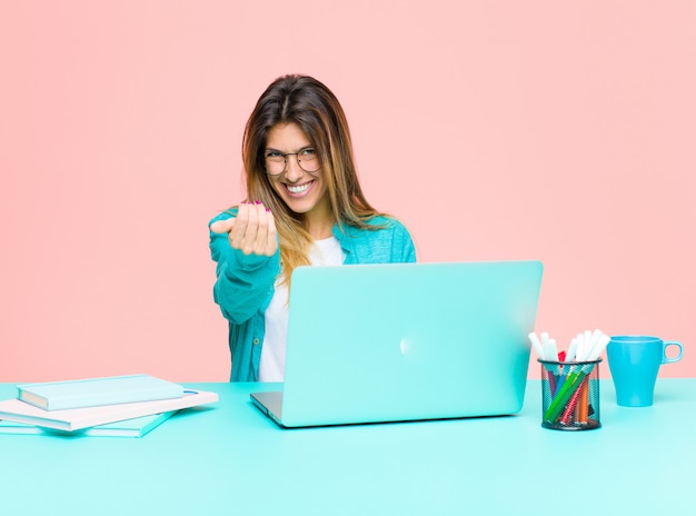 Mulher jovem e bonita trabalhando com um laptop se sentindo feliz, bem-sucedida e confiante, enfrentando um desafio e dizendo: traga-o! ou recebê-lo