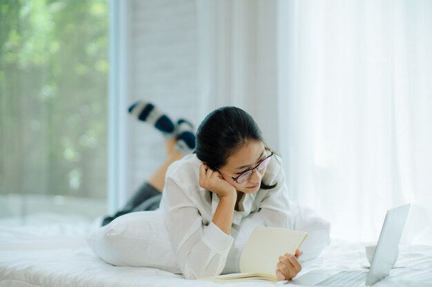 Mulher jovem e bonita trabalhando na cama, ela palestra e olhando o caderno. foco suave e suave