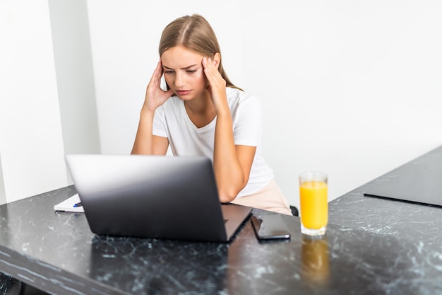 Mulher jovem e bonita triste na cozinha dentro de casa em casa usando um laptop