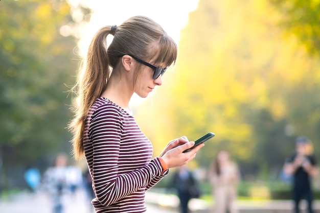 Mulher jovem e bonita usando seu telefone celular em um dia quente de verão ao ar livre.