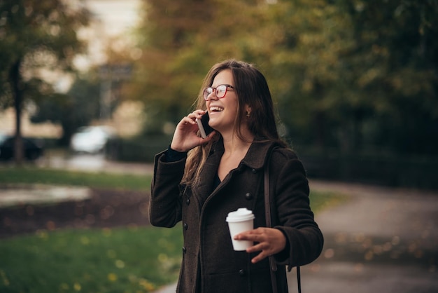 Mulher jovem e bonita usando smartphone e tomando café para viagem