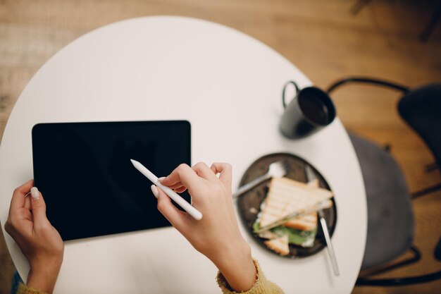 Mulher jovem e bonita usando tablet digital na mesa do café com uma xícara de café