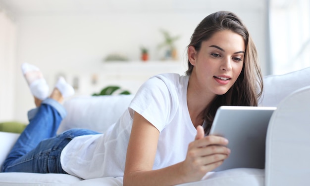 Mulher jovem e bonita usando tablet sentado no sofá em casa na sala de estar.