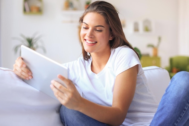 Mulher jovem e bonita usando tablet sentado no sofá em casa na sala de estar