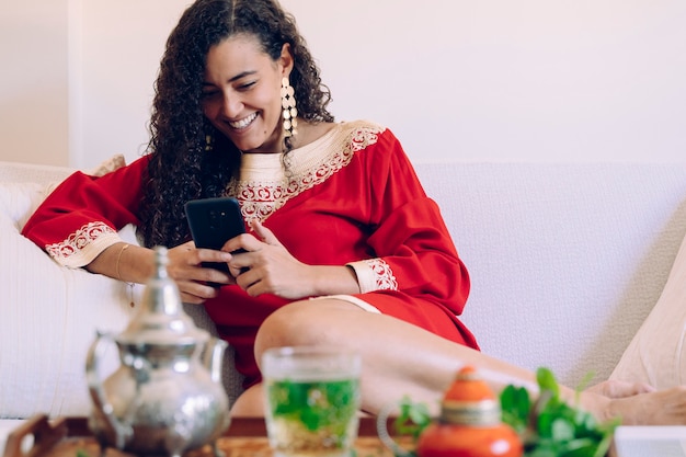 Mulher jovem e bonita usando um smartphone em casa e bebendo chá