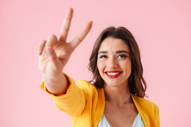 Mulher jovem e bonita vestindo roupas coloridas em pé isolado sobre o rosa, mostrando paz