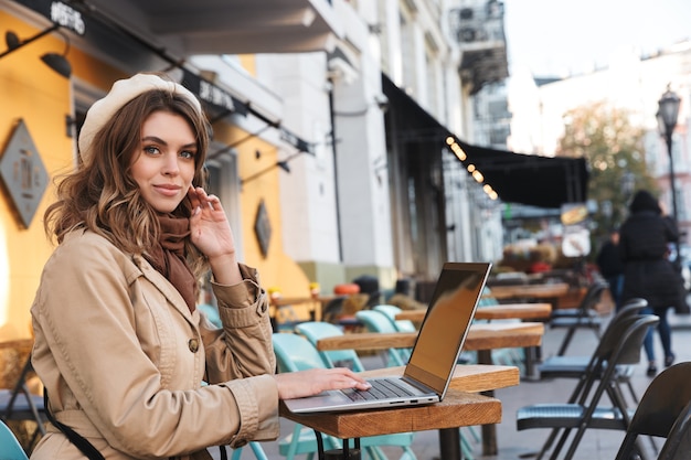 Mulher jovem e bonita vestindo um casaco usando um laptop enquanto está sentado no café