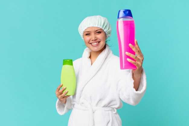 Mulher jovem e bonita vestindo um roupão de banho e segurando uma garrafa de produto limpa