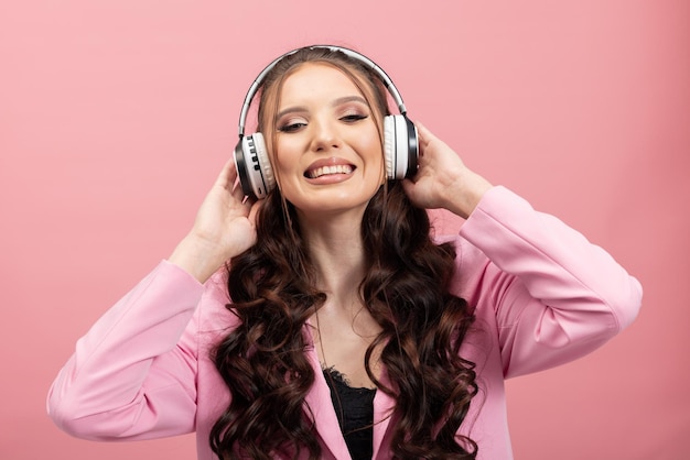 Mulher jovem e bonita vestindo uma jaqueta com fones de ouvido sem fio, ouvindo música em um rosa