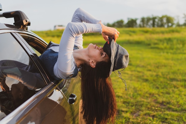 Mulher jovem e bonita viaja de carro inclinando-se para fora da janela e se divertindo