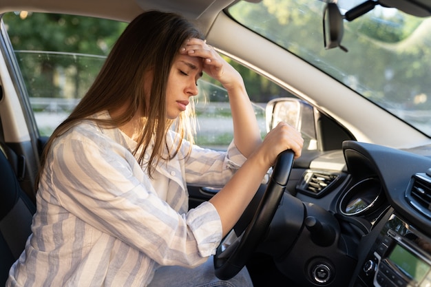 Foto mulher jovem e cansada, motorista de carro, sofre de dor de cabeça ou enxaqueca dentro do veículo, toque na testa