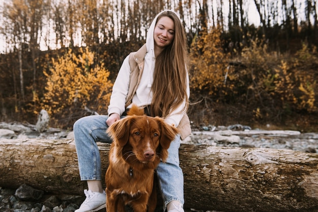 Mulher jovem e cão retriever caminham na margem do rio na temporada de outono