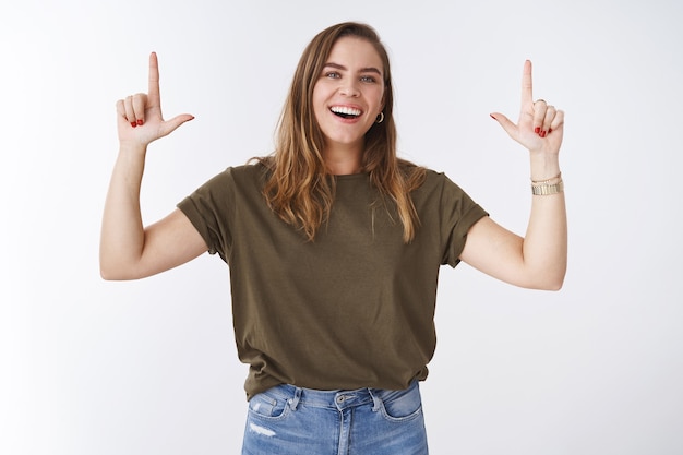 Mulher jovem e carismática, jovem e bonita, caucasiano, menina, modelo, vestindo jeans verde-oliva, sorrindo, rindo casualmente amigável, olhando a câmera levantando o dedo indicador apontando para cima publicidade promocional