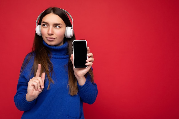 Mulher jovem e concentrada muito séria, usando um suéter azul isolado sobre um fundo vermelho