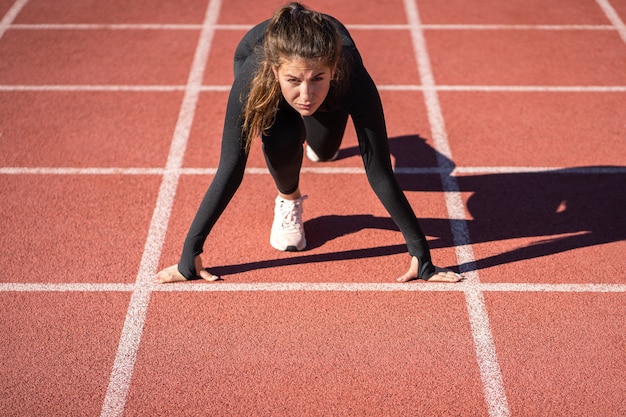 Mulher jovem e confiante em forma de velocista em uma esteira de borracha ou em uma pista de corrida se preparando para começar a correr