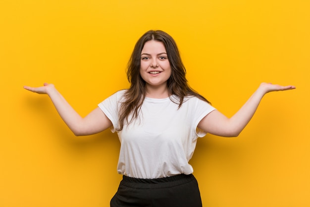 Mulher jovem e curvilínea plus size faz escala com os braços, sente-se feliz e confiante.