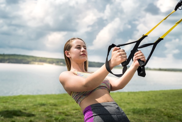 Mulher jovem e desportiva fazendo exercícios de TRX