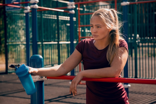 Mulher jovem e desportiva segurando um agitador de água depois de um treino no campo esportivo