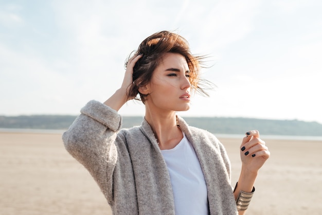 Mulher jovem e elegante com um casaco em pé e posando perto do mar