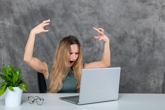 Mulher jovem e elegante de vestido cinza posando na frente de um laptop e uma flor verde