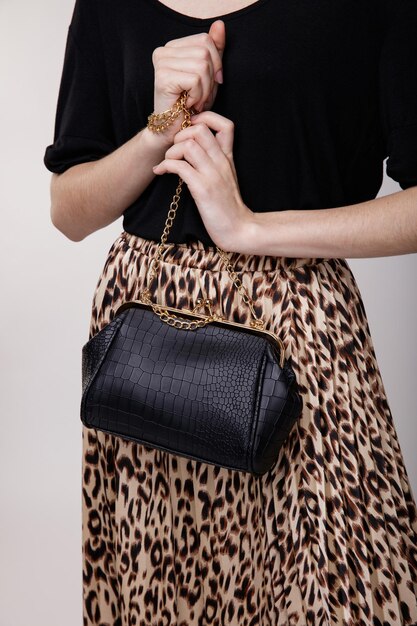 mulher jovem e elegante em saia longa de leopardo, top preto, chapéu, bolsa em fundo branco