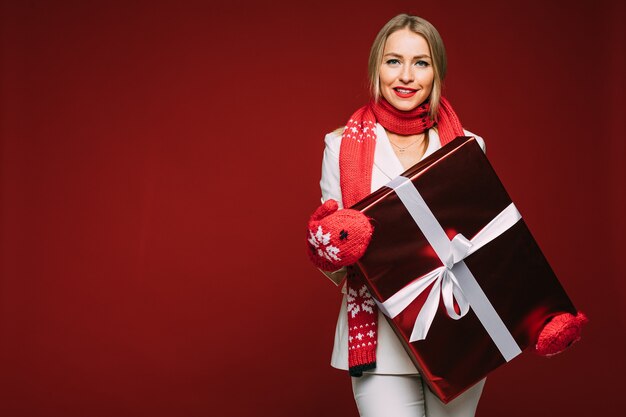 Mulher jovem e elegante em um terno elegante e luvas segurando uma grande caixa de presente de Natal e olhando para a câmera. Conceito de férias