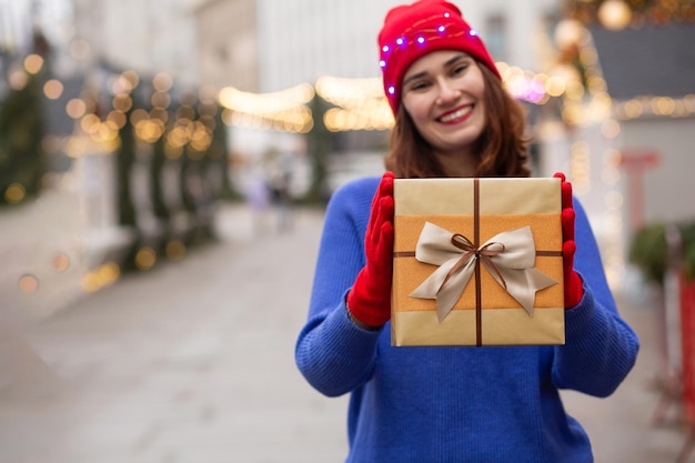 Mulher jovem e encantadora dando uma caixa de presente na feira de Natal. Espaço para texto