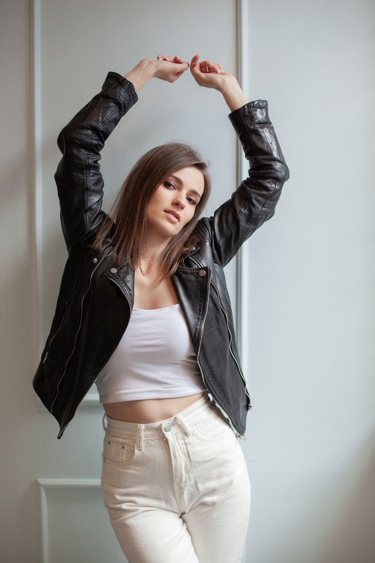 Foto mulher jovem e encantadora posando de jaqueta de couro preta e calça jeans branca sobre um fundo branco. beleza, moda.