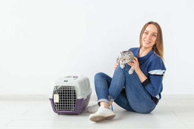 Mulher jovem e encantadora segura nas mãos seu lindo gato escocês cinza sentado no chão