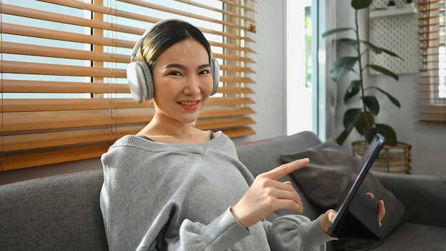 Mulher jovem e encantadora usando fone de ouvido assistindo vídeo navegando na internet ou fazendo compras on-line via tablet digital