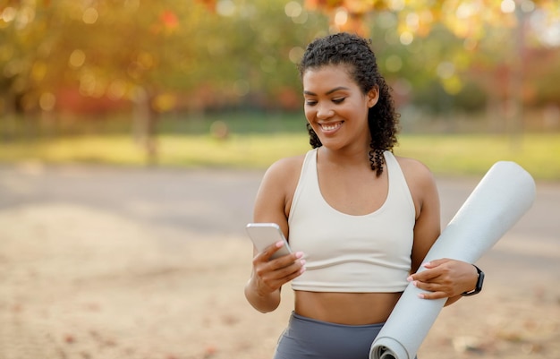 Foto mulher jovem e esportiva com tapete de ginástica rolando smartphone ao ar livre