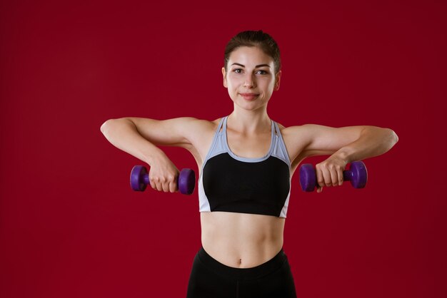 Mulher jovem e esportiva em roupas esportivas com halteres na mão em uma mulher vermelha que pratica esportes